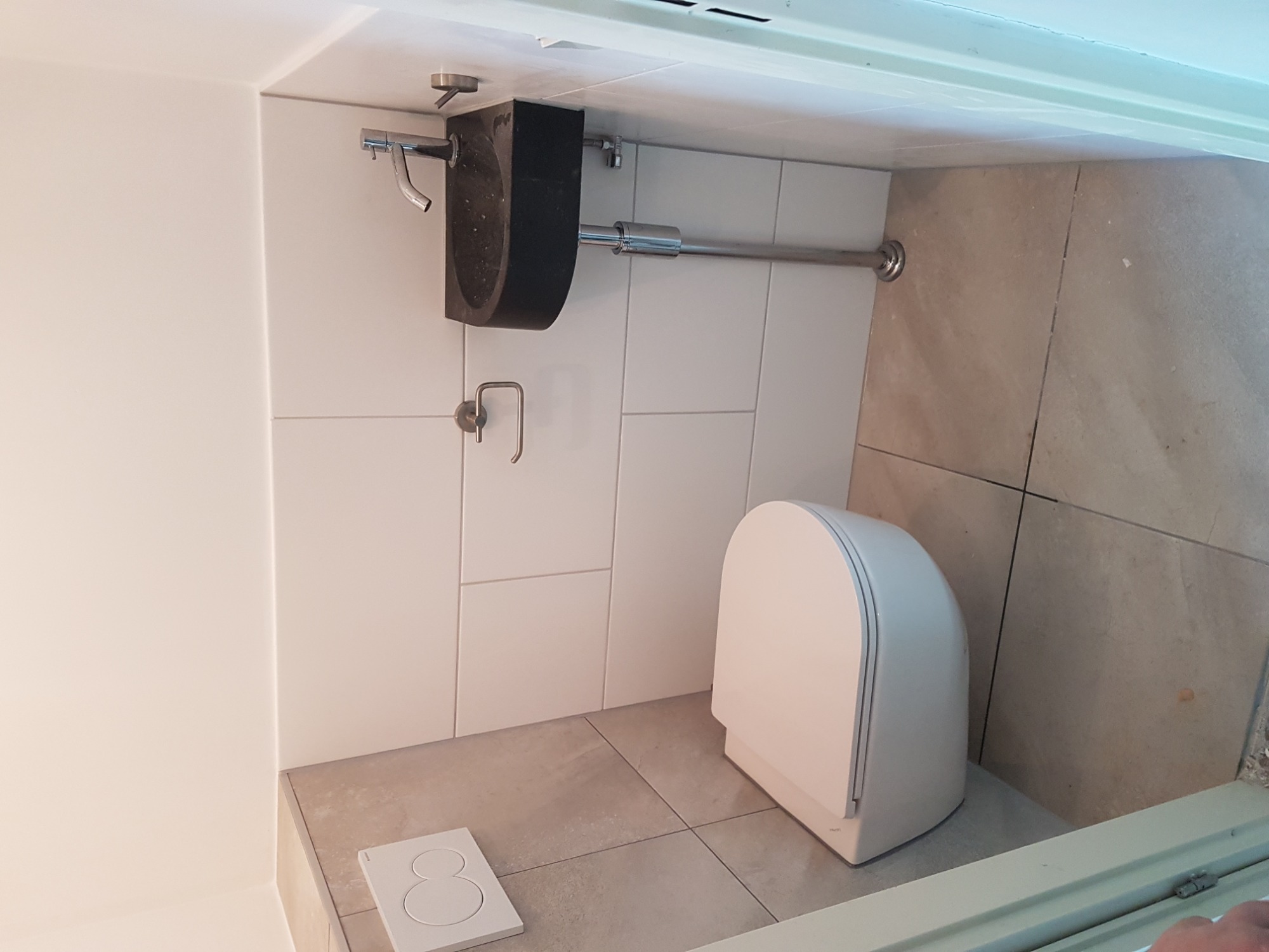 Nowoczesna łazienka z wiszącą, czarną umywalką z kamienia, białą toaletą podwieszaną i beżowymi płytkami podłogowymi oraz białymi płytkami ściennymi.