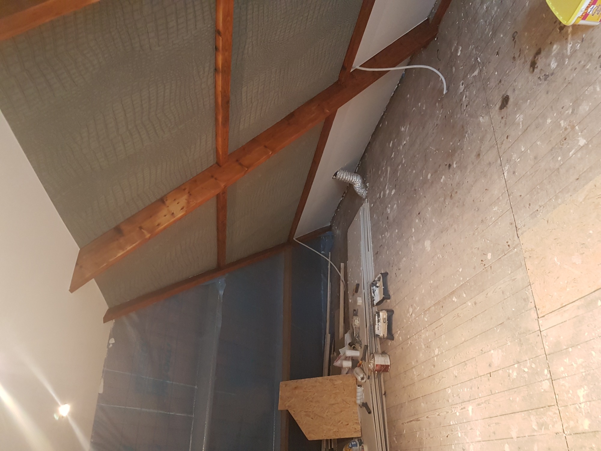 Poddasze w trakcie prac w Kętach: widoczne drewniane belki stropowe, ocieplenie wełną mineralną, fragment ściany z płyt kartonowo-gipsowych oraz podłoga z desek z widocznymi śladami farby.