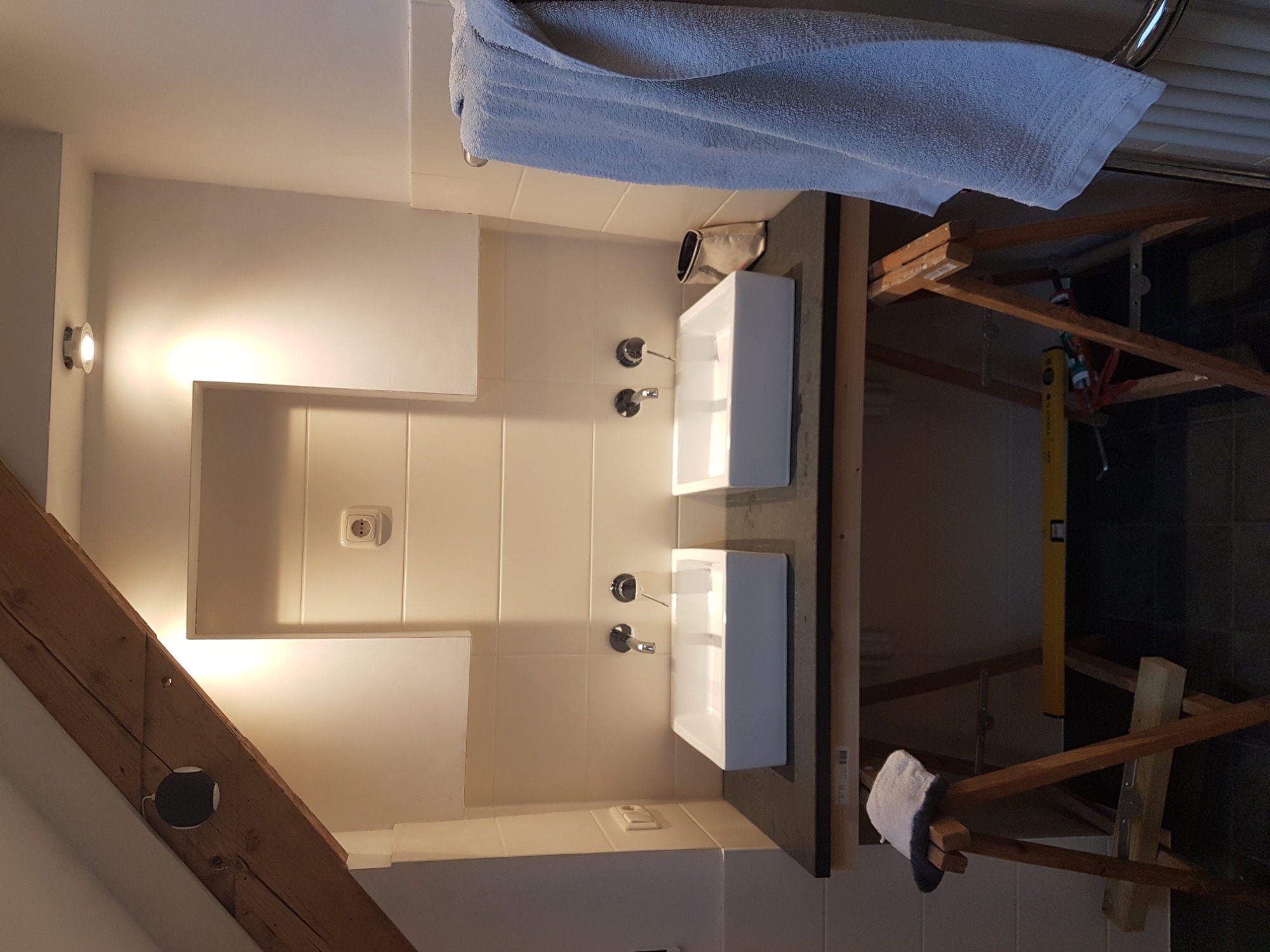 Dwie białe, prostokątne umywalki zamontowane na ciemnym blacie w łazience w trakcie prac wykończeniowych, widoczne rusztowanie i poziomica.