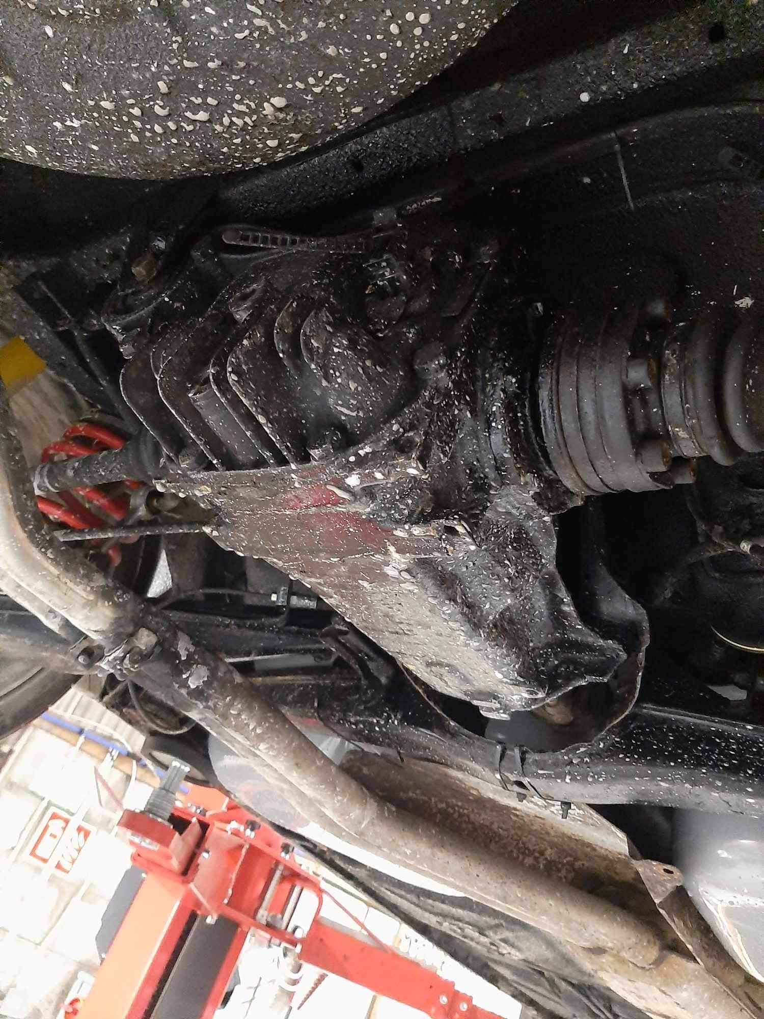 Widok podwozia samochodu na podnośniku, ze szczególnym uwzględnieniem tylnego mostu, sprężyny zawieszenia pomalowanej na czerwono i elementów układu wydechowego, pokrytych substancją antykorozyjną.