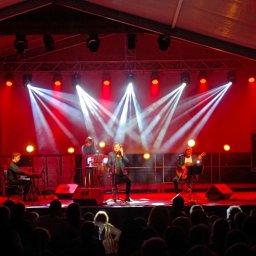 OSWIETLIMYWSZYSTKO.PL - Zespół muzyczny na scenie oświetlonej czerwonymi i białymi światłami podczas występu dla publiczności.