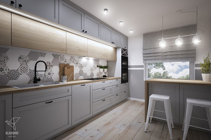 Szara kuchnia z drewnianymi blatami i heksagonalnymi płytkami w odcieniach szarości i bieli, czarna bateria kuchenna i minimalistyczne oświetlenie podszafkowe, widoczne dwa białe hokery przy...