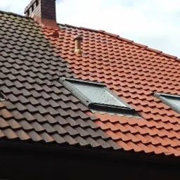 Częściowo wyczyszczony dach z dachówki ceramicznej z trzema oknami dachowymi, ukazujący różnicę w wyglądzie przed i po czyszczeniu, z widocznym kominem i wentylacją.