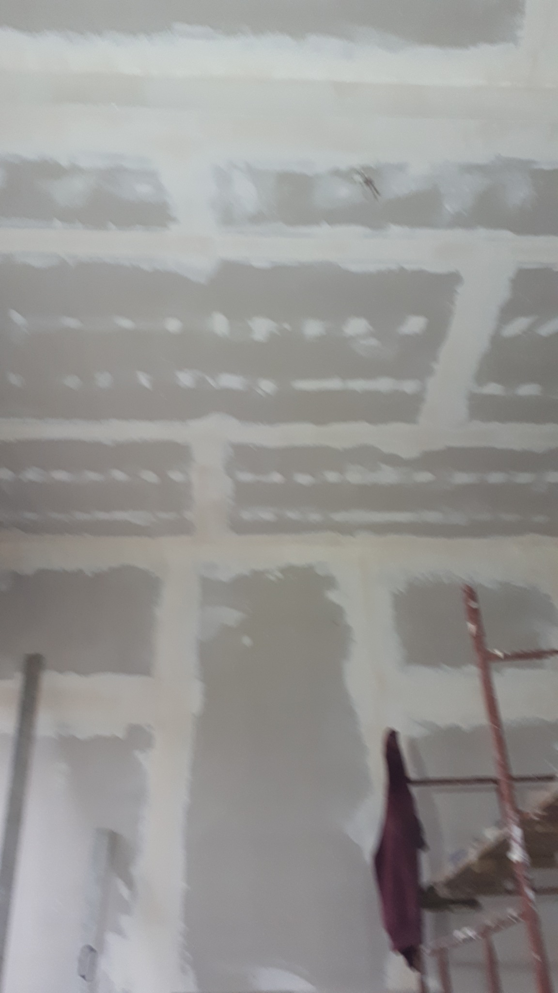 Sufit z płyt kartonowo-gipsowych w trakcie montażu, widoczne łączenia wymagające szpachlowania, fragment rusztowania z czerwoną szmatą w prawym dolnym rogu.