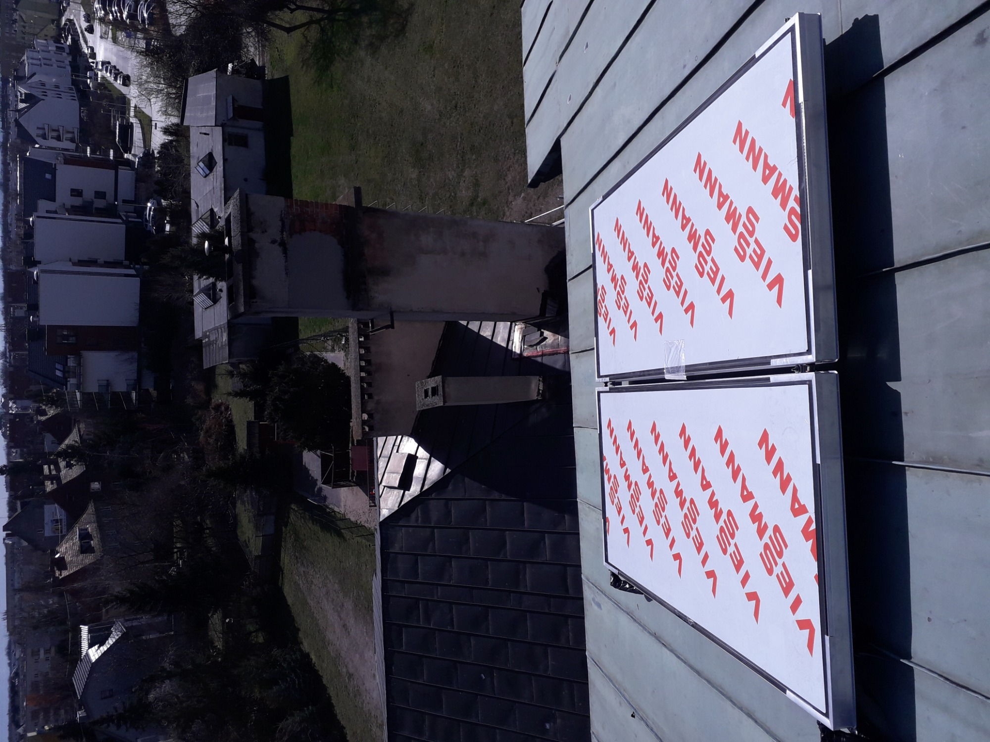 Dwa panele słoneczne marki Viessmann na dachu domu, widok z góry na komin i okoliczną zabudowę.