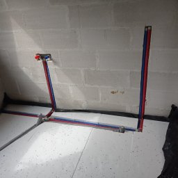 Sypex - Instalacja ogrzewania podłogowego z rurami PEX w kolorze niebieskim i czerwonym, ułożonymi na białym styropianie, przy ścianie z betonu komórkowego.