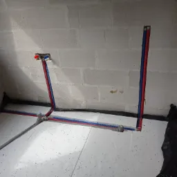 Instalacja ogrzewania podłogowego z rurami PEX w kolorze niebieskim i czerwonym, ułożonymi na białym styropianie, przy ścianie z betonu komórkowego.