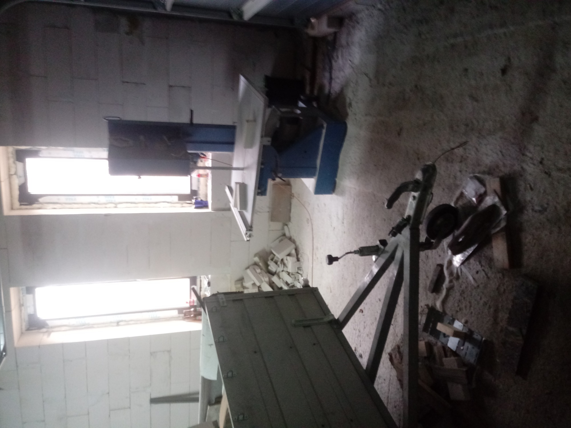 Wnętrze w trakcie budowy domu z bloczków, widoczna piła do cięcia bloczków, przyczepka i porozrzucane materiały budowlane.