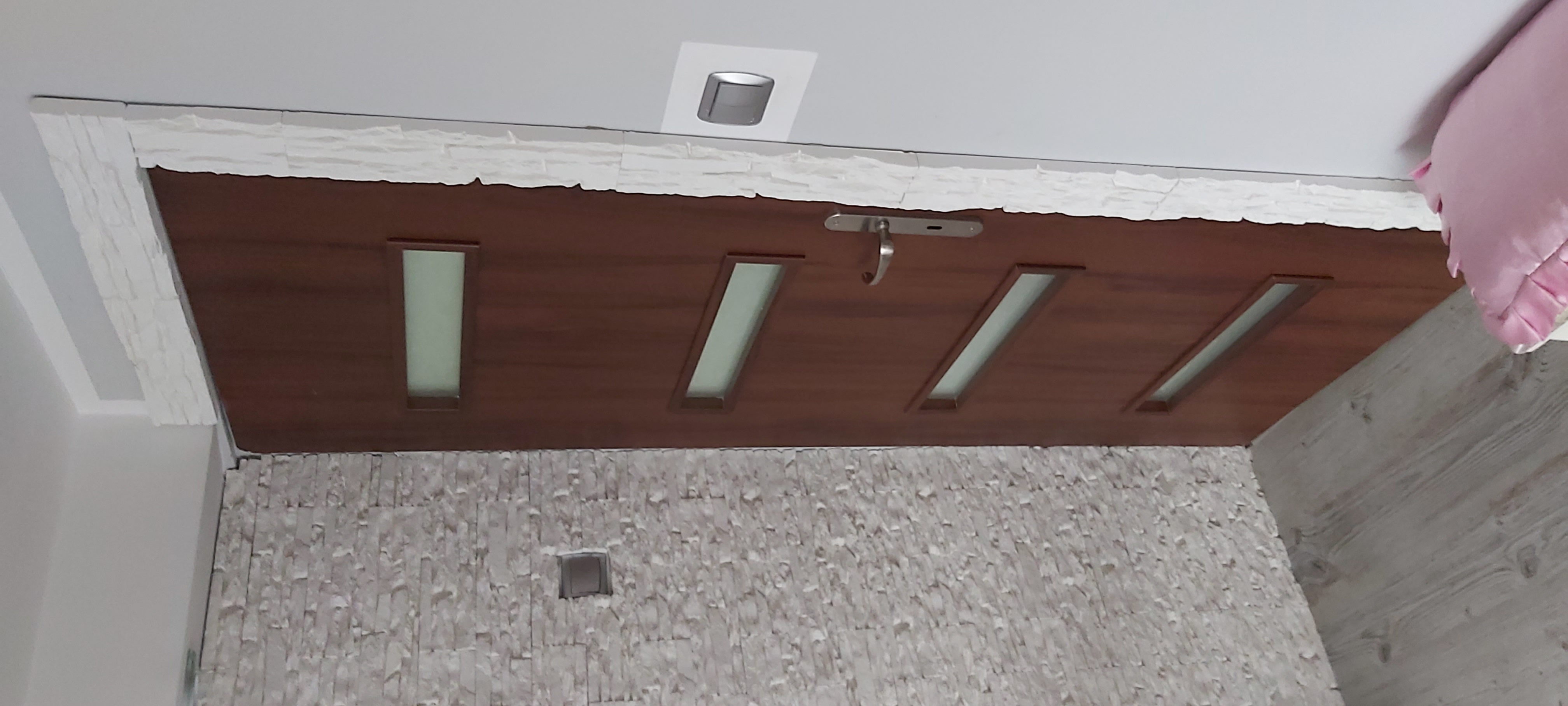 Drewnopodobny sufit z czterema podłużnymi przeszkleniami i metalowym haczykiem, wykończony dekoracyjnym kamieniem, widok z dołu.