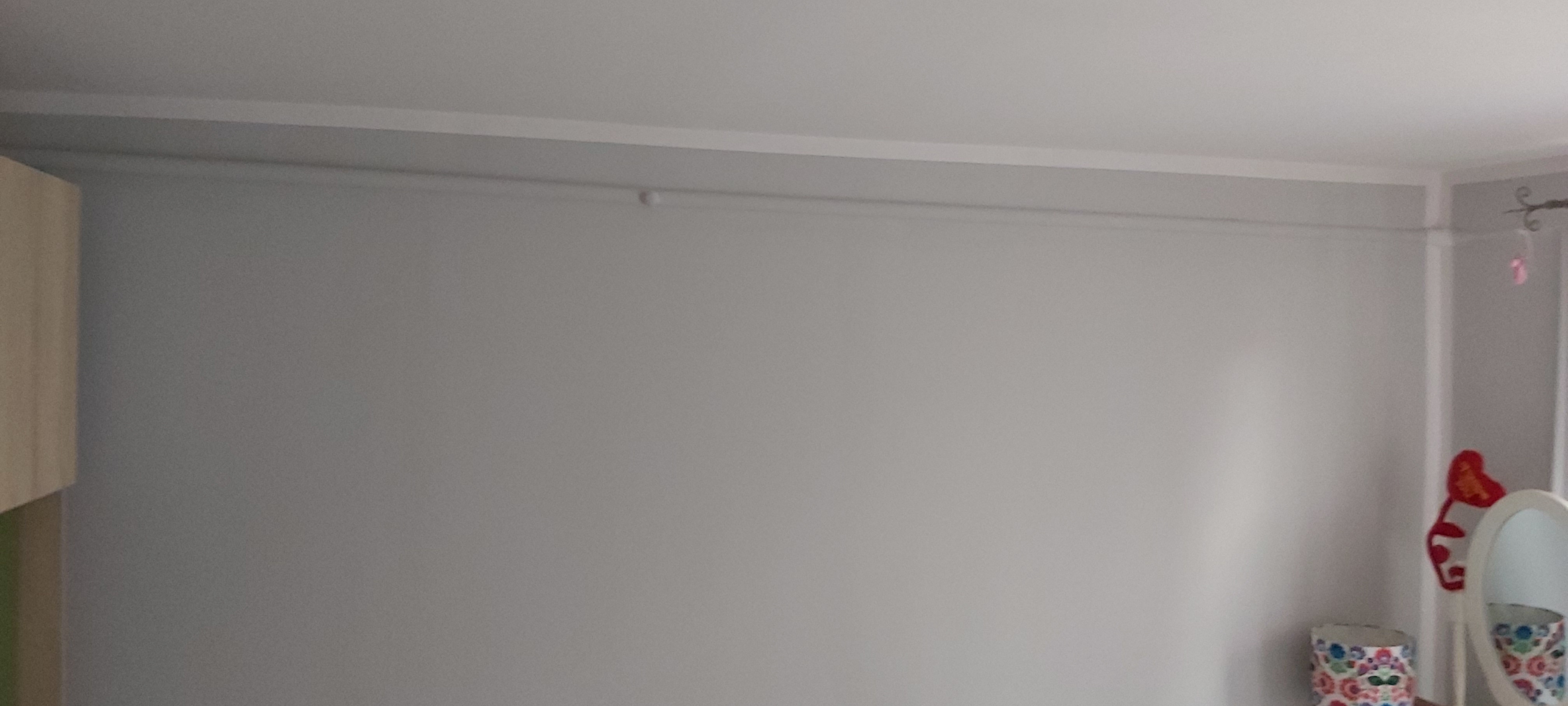 Szara ściana po malowaniu z widoczną listwą przysufitową i gładzią, z elementami dekoracyjnymi w rogu pokoju.