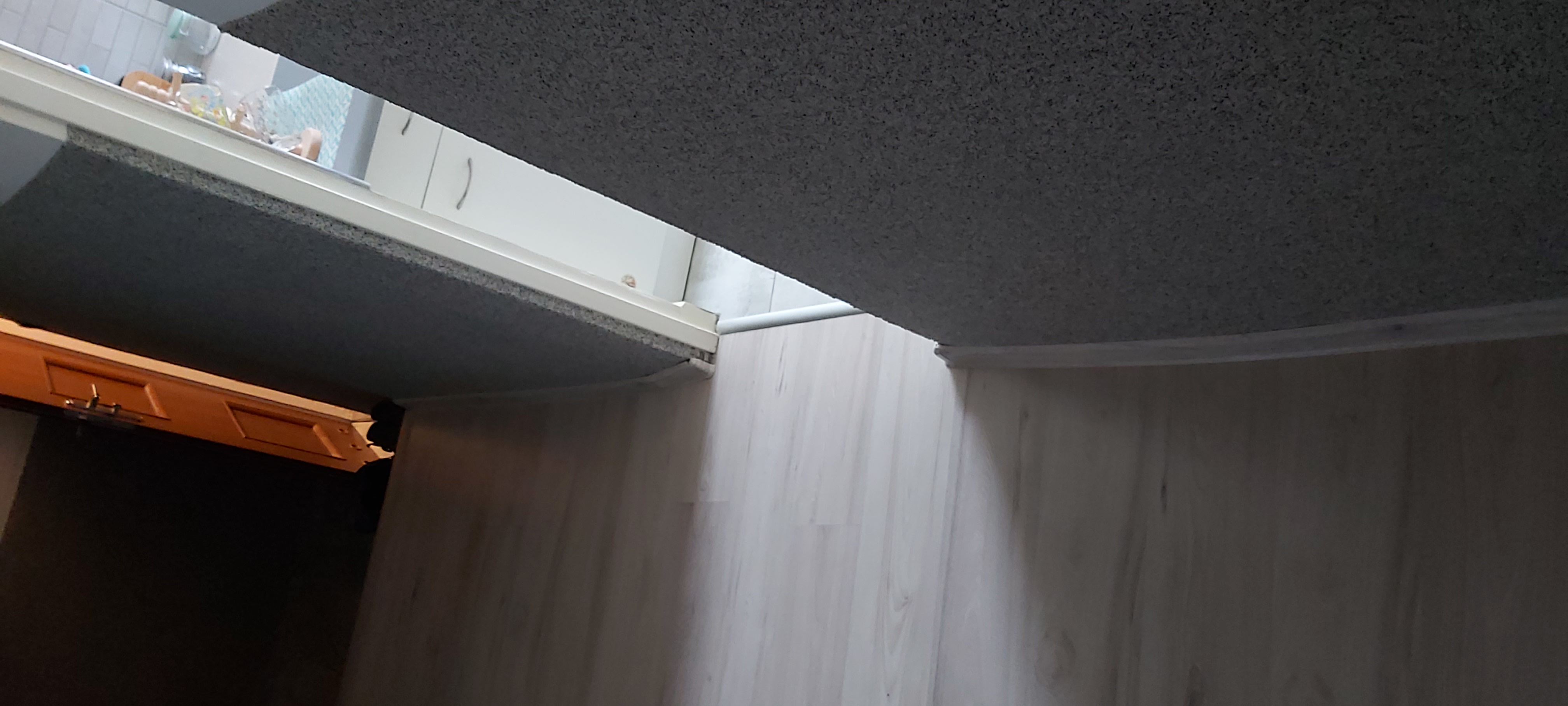 Fragment łazienki po remoncie: widoczny sufit z fakturą, białe panele ścienne i fragment szafki pod umywalką z jasnego drewna.