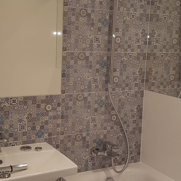 Ukończona łazienka z wzorzystymi, patchworkowymi płytkami w odcieniach szarości i błękitu, widoczna umywalka z chromowaną baterią i fragment wanny.