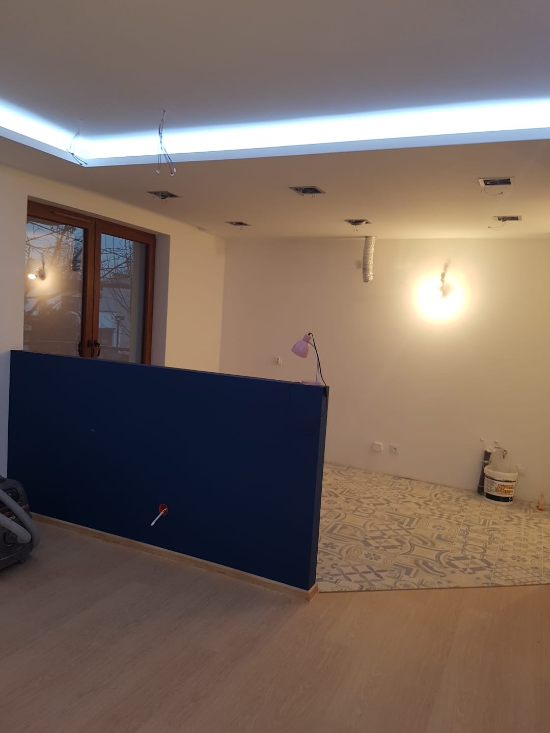 Wnętrze w trakcie remontu: położone płytki podłogowe o wzorze geometrycznym, pomalowana na granatowo ścianka działowa, widoczne puszki elektryczne i kable wystające z sufitu, przygotowane...