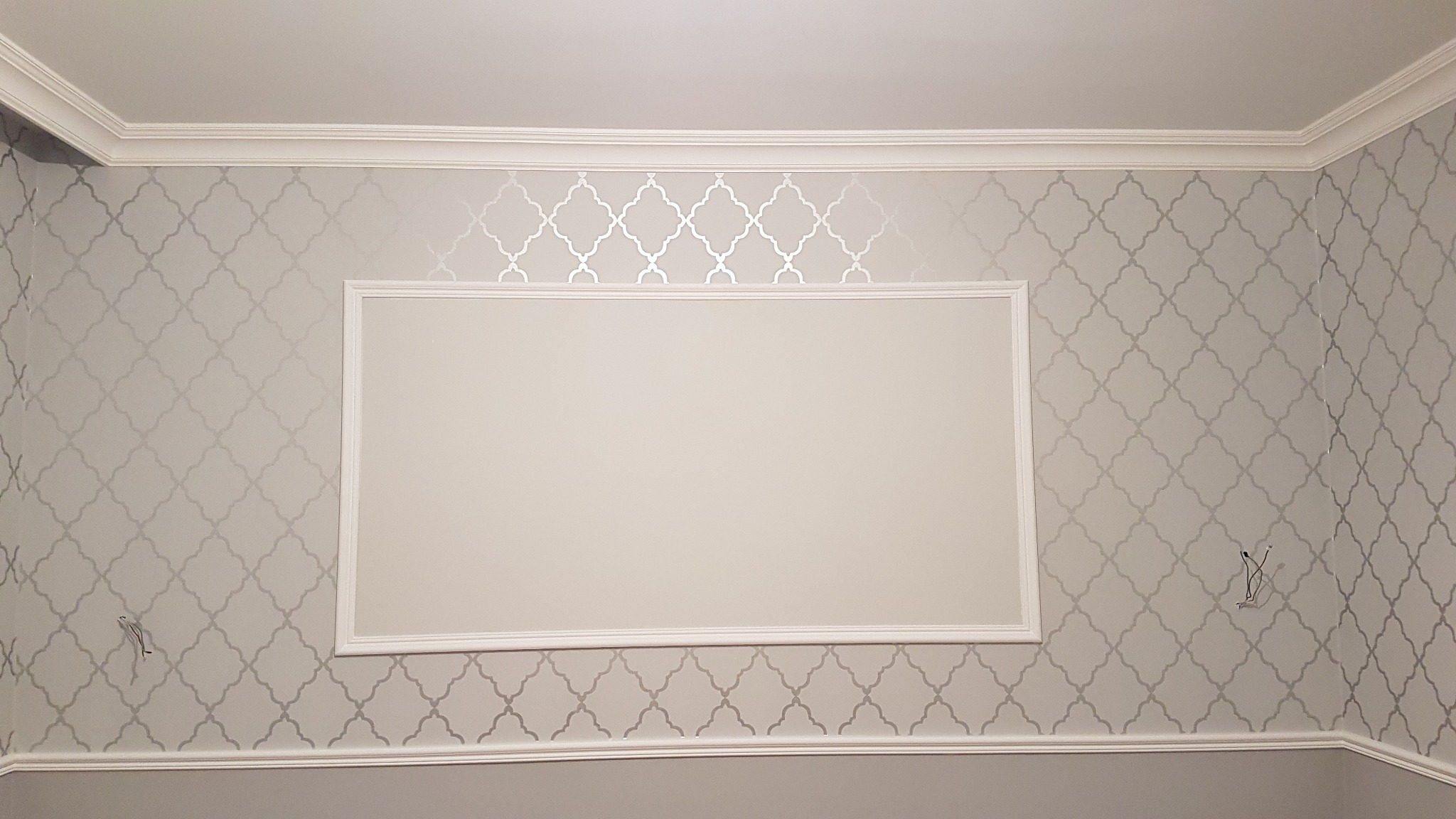 Ściana z szarym wzorem marokańskim, obramowana listwami dekoracyjnymi i pustym, prostokątnym polem na ścianie, z widocznymi przewodami elektrycznymi.