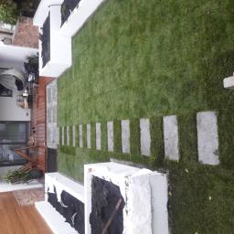 Vasyl Vakula - Widok z góry na ogród po remoncie z równo ułożonym trawnikiem, ścieżką z płyt betonowych i podwyższonymi rabatami kwiatowymi, w tle taras z meblami ogrodowymi.