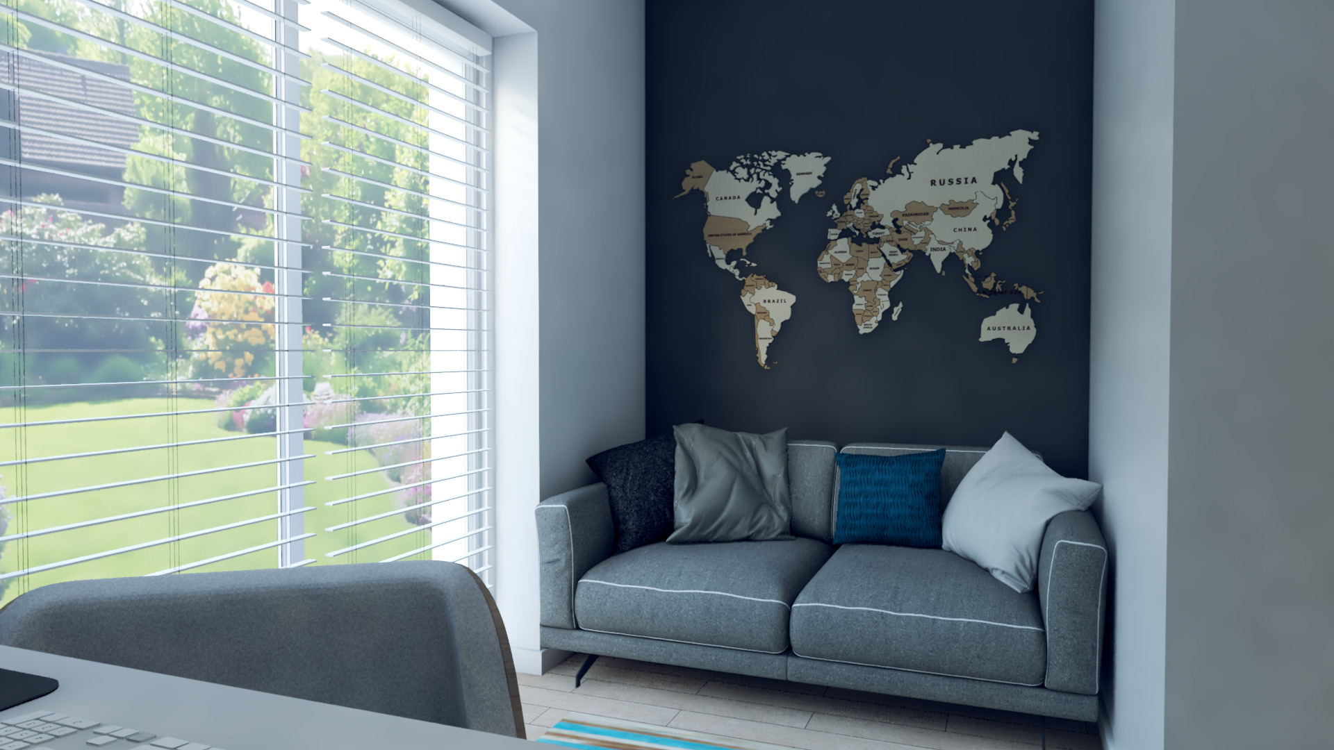 Szara sofa z poduszkami pod drewnianą mapą świata na ciemnej ścianie, widok zza biurka i krzesła przy oknie z żaluzjami.