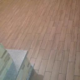 Ułożona podłoga z płytek imitujących drewno w odcieniach beżu, z fragmentem kamiennej obudowy. Widok z góry, diagonalne ułożenie płytek.