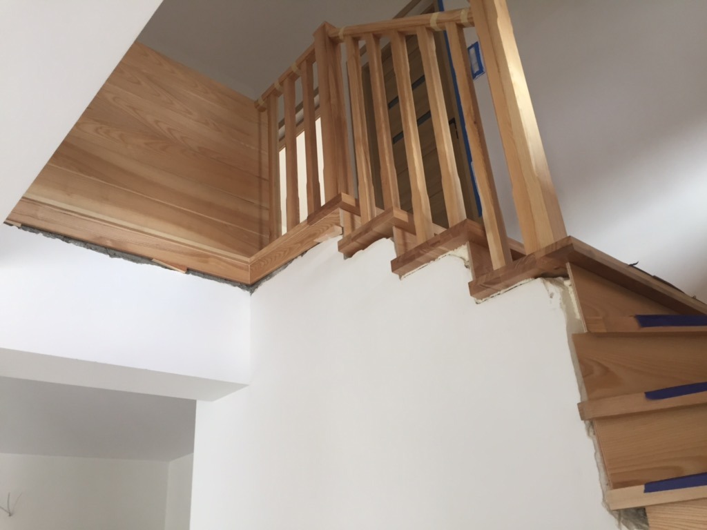 Montaż drewnianych schodów z balustradą i obudową ściany, widoczne niedoskonałości wykończenia i zabezpieczenia taśmą malarską.