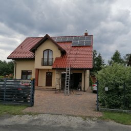 MAWBUD plus Marek Wojtasik - Dom jednorodzinny z czerwoną dachówką, na której zamontowane są panele słoneczne, widoczne rusztowanie i drabina, sugerujące trwający montaż instalacji.