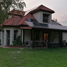 MAWBUD plus Marek Wojtasik - Dom jednorodzinny z panelami słonecznymi na dachu i zadaszeniu tarasu, widok z ogrodu w lekko pochmurny dzień.