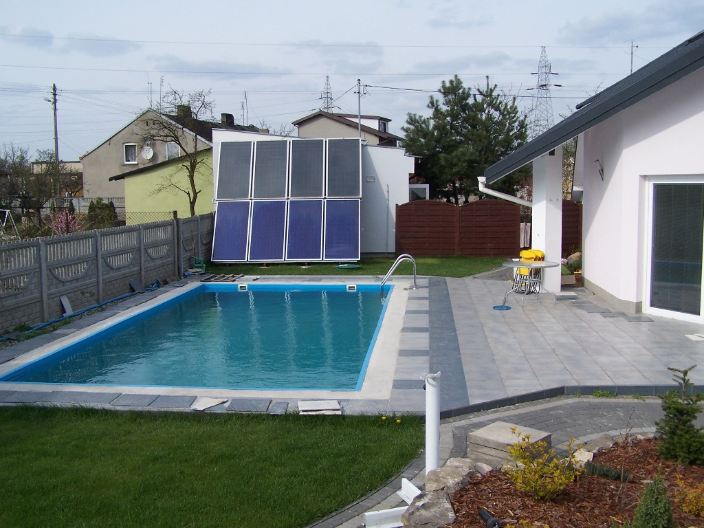 Basen z zainstalowanymi kolektorami słonecznymi w Konstantynowie Łódzkim, widok na posesję z szarym ogrodzeniem i domami w tle.