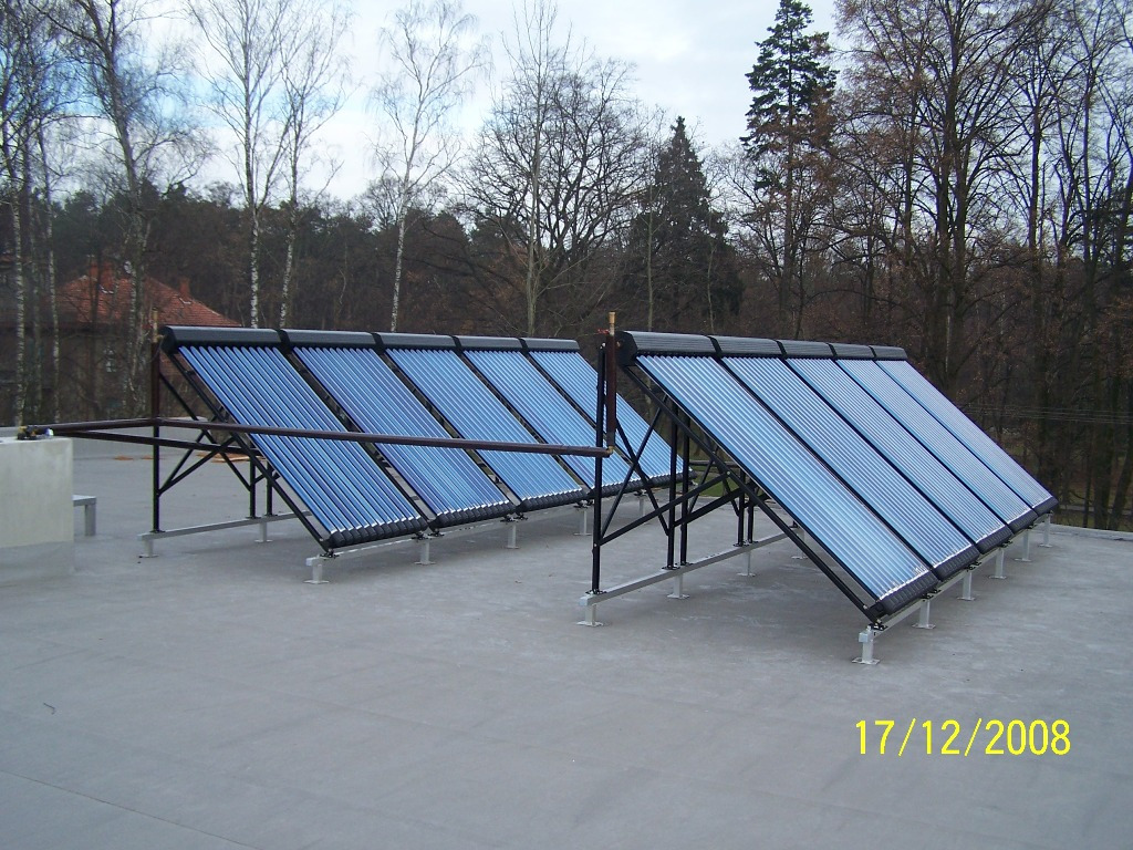 Dwa rzędy kolektorów słonecznych rurowych zamontowane na płaskim dachu budynku, z datą 17/12/2008 widoczną w prawym dolnym rogu, drzewa w tle.
