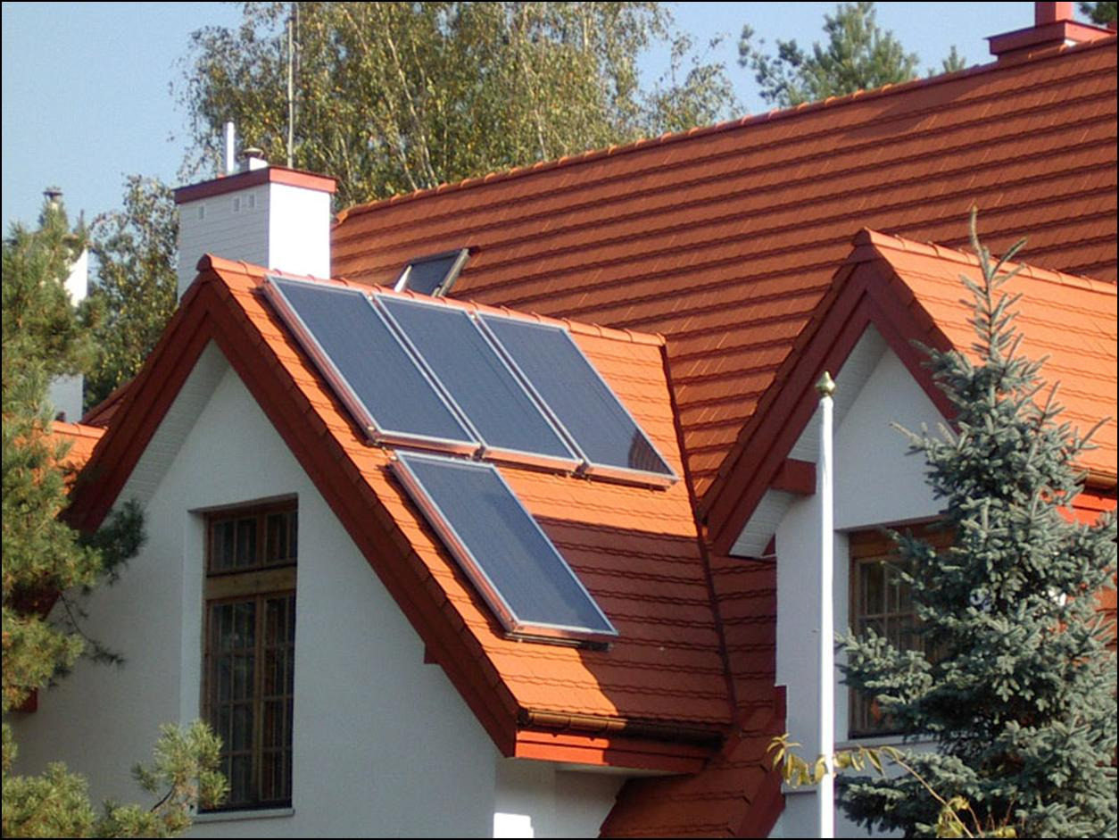 Czerwony dach domu jednorodzinnego z zamontowanymi panelami słonecznymi, widok z dołu na tle drzew.