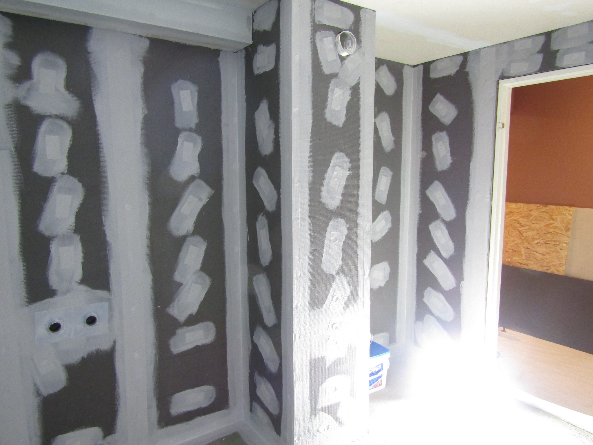 Przygotowanie ścian pod glazurę: siatka zatopiona w kleju, wzmocnione narożniki, widoczne puszki elektryczne. Etap prac wykończeniowych w łazience.