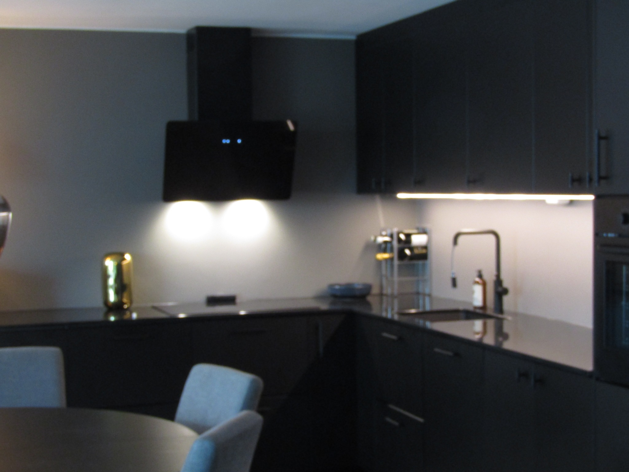 Nowoczesna, czarna zabudowa kuchenna z oświetleniem LED w Hovik. Minimalistyczny design z ciemnymi frontami i złotym akcentem dekoracyjnym na blacie.