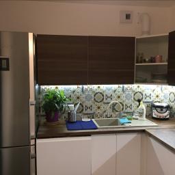 NETMAX Sp. z o.o. - Nowoczesna kuchnia z białymi szafkami, drewnianymi blatami, mozaiką nad zlewem, i srebrną lodówką Liebherr po lewej stronie.