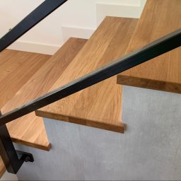 ELBOWOOD Andzej Borkowski - Drewniane schody z czarną, metalową balustradą, widok z góry. Stopnie z jasnego drewna, boki schodów w odcieniach szarości. Minimalistyczny design.