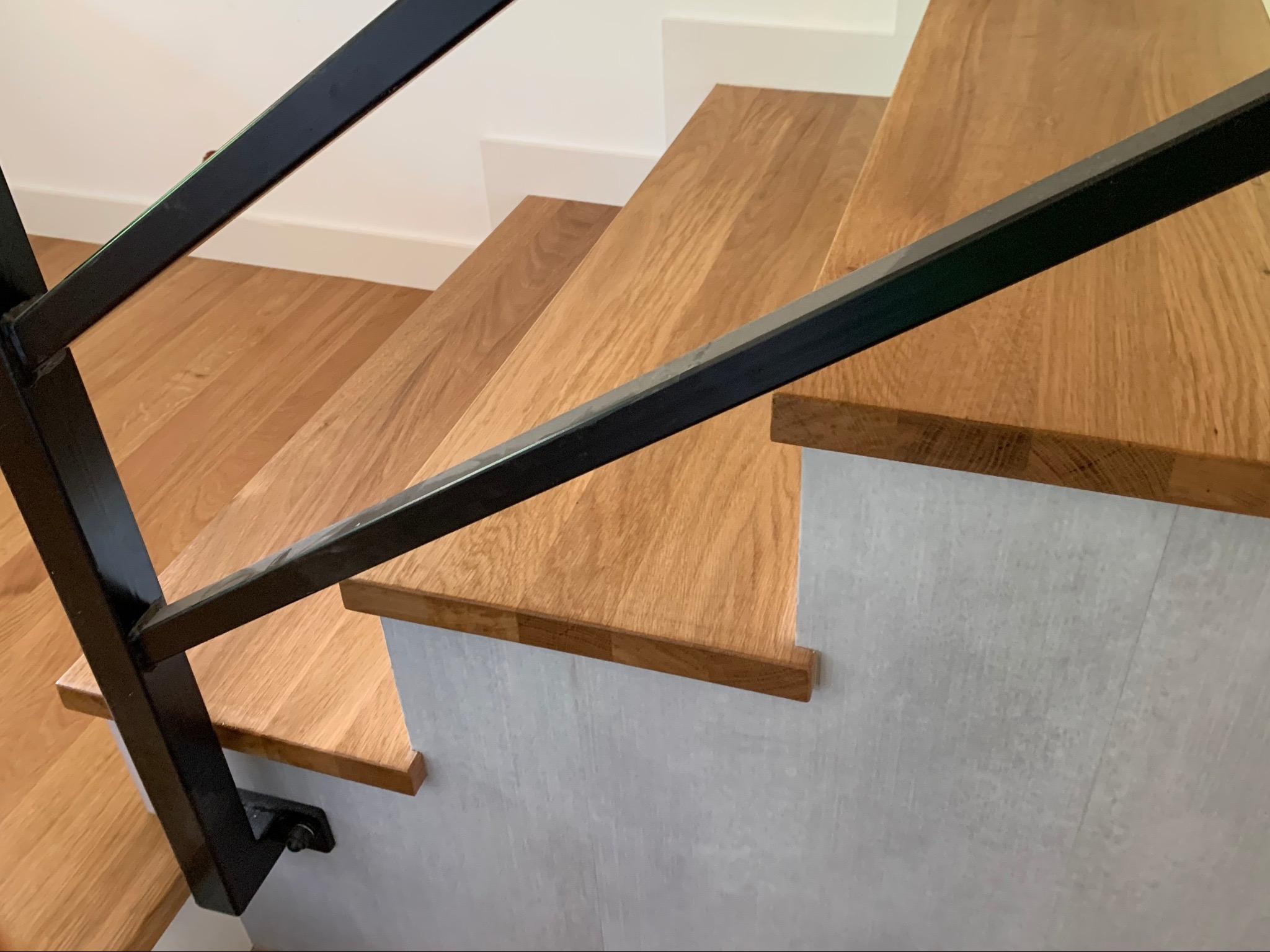 Drewniane schody z czarną, metalową balustradą, widok z góry. Stopnie z jasnego drewna, boki schodów w odcieniach szarości. Minimalistyczny design.