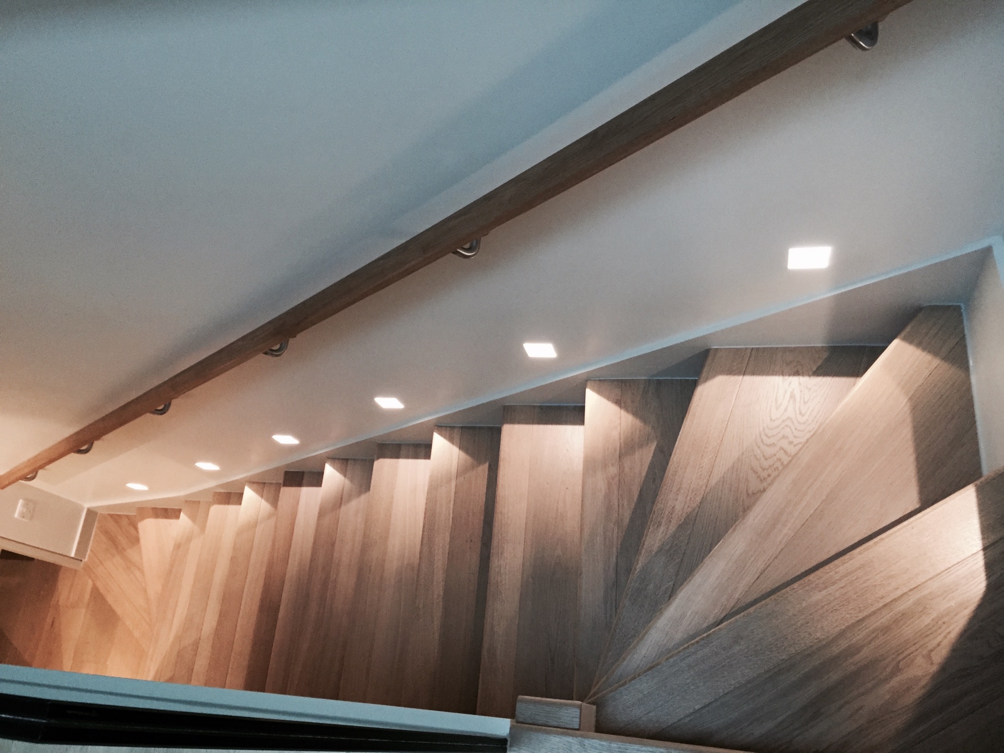 Drewniane schody kręcone z oświetleniem punktowym w suficie i drewnianą poręczą, widok z góry.