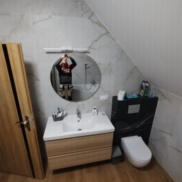 Usługi Remontowo-Budowlane Anna Wojtkiewicz - Wykończona łazienka na poddaszu z umywalką, toaletą i lustrem; odbicie fotografa w lustrze.