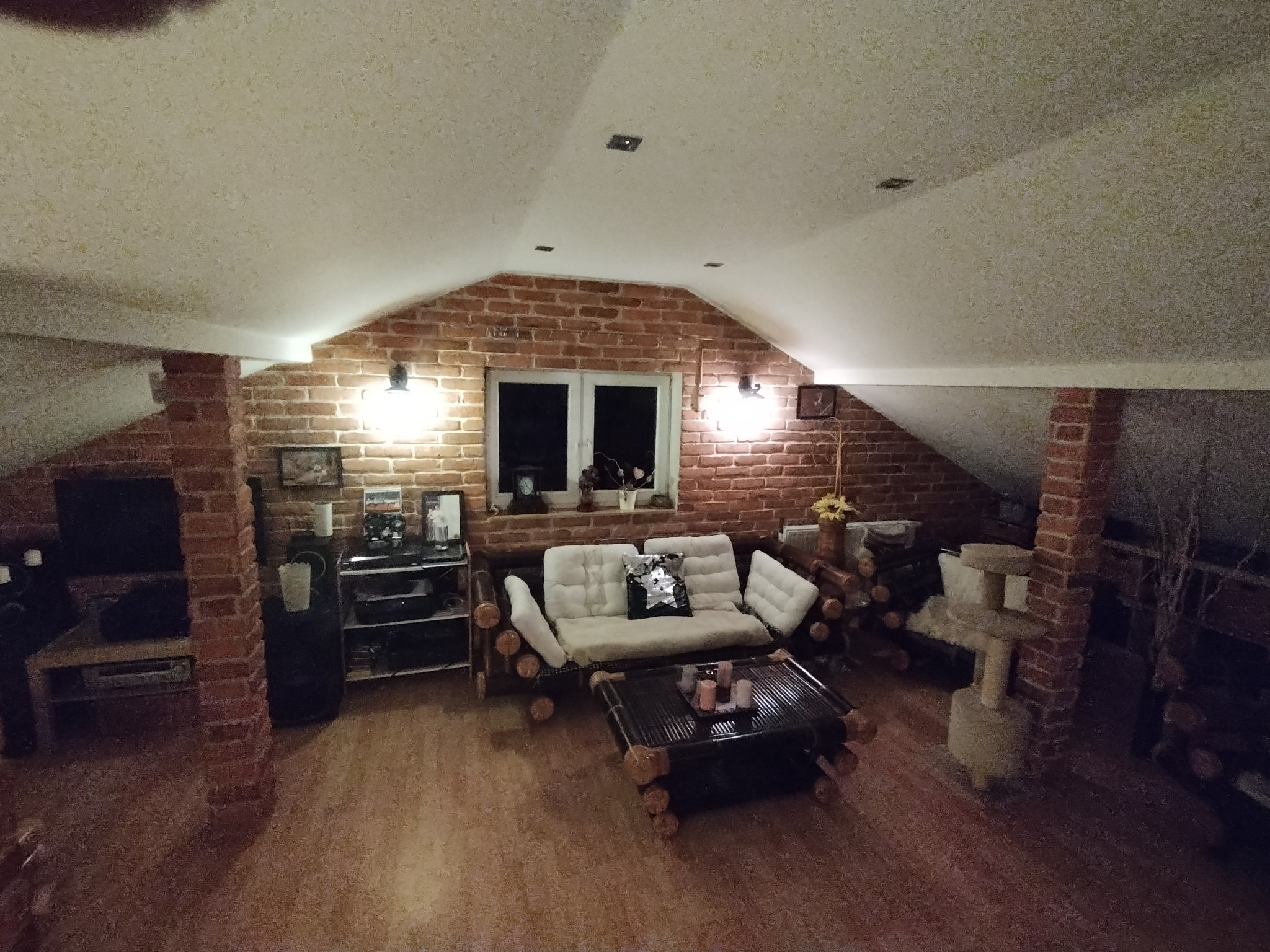 Przytulne poddasze z ceglaną ścianą, drewnianymi meblami i oświetleniem punktowym.