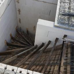 Staska Bau Rem - Wewnętrzna konstrukcja schodów spiralnych w trakcie budowy, widoczne białe bloczki, drewniane podpory i zbrojenie.