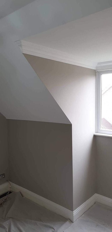 Świeżo pomalowane poddasze z oknem, ściany w odcieniach szarości i bieli, widoczna listwa przypodłogowa i zabezpieczona folią podłoga.