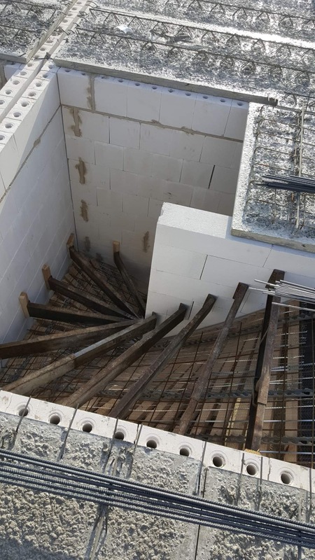 Wewnętrzna konstrukcja schodów spiralnych w trakcie budowy, widoczne białe bloczki, drewniane podpory i zbrojenie.