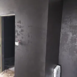 Ściana w ciemnym, grafitowym kolorze z efektem dekoracyjnym, widoczne zabezpieczenia podłogi i narożnika, fragment otworu drzwiowego.