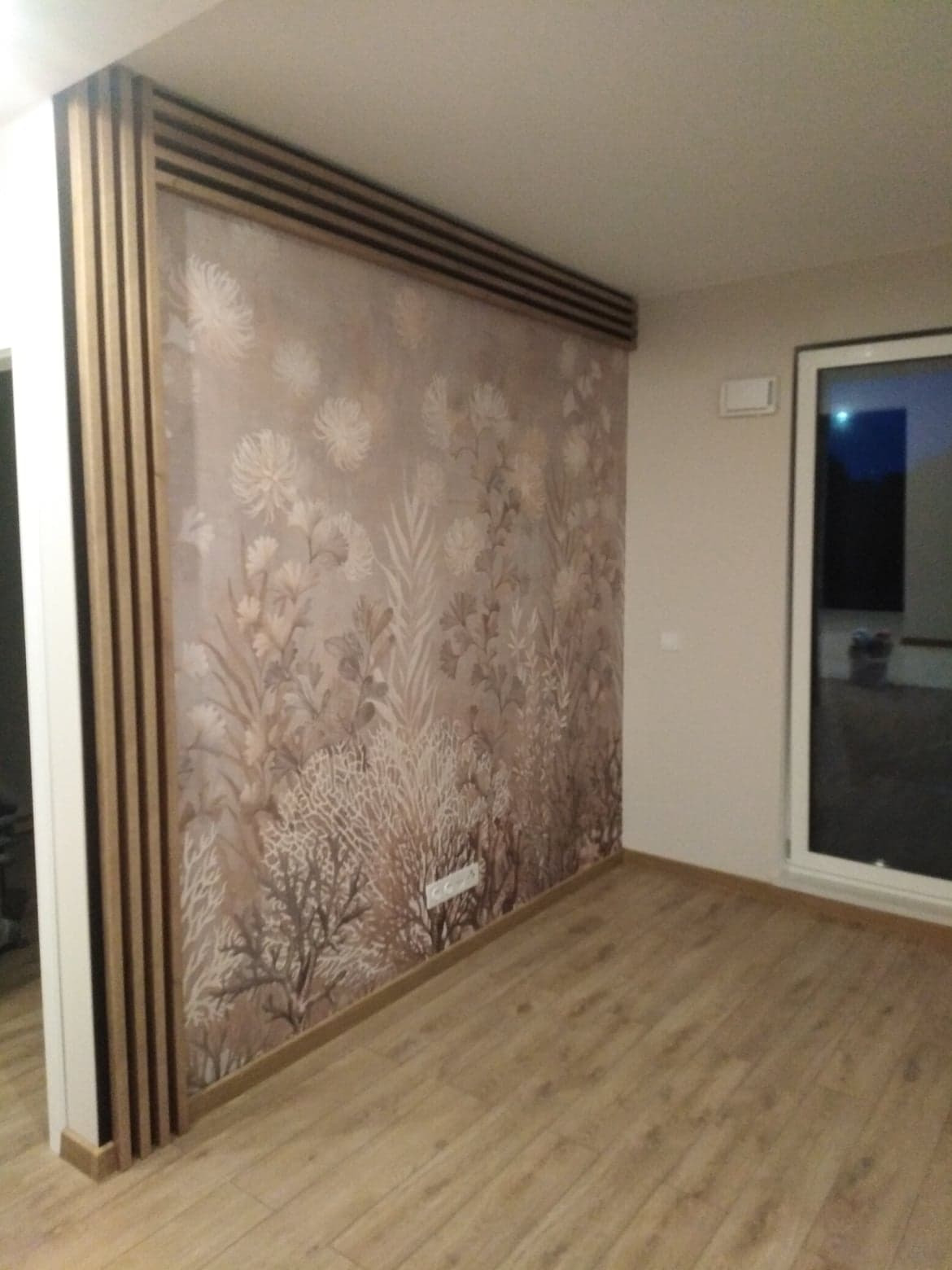 Pokój po remoncie z tapetą w kwiaty i drewnianymi listwami dekoracyjnymi na ścianie oraz podłodze z paneli.