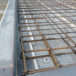 KRZYSZTOF HABRYŁO HAB-KRIS - Zbrojenie płyty fundamentowej z widocznymi elementami izolacji termicznej i szalunkiem. Detal z bliska ukazuje siatkę z prętów zbrojeniowych.