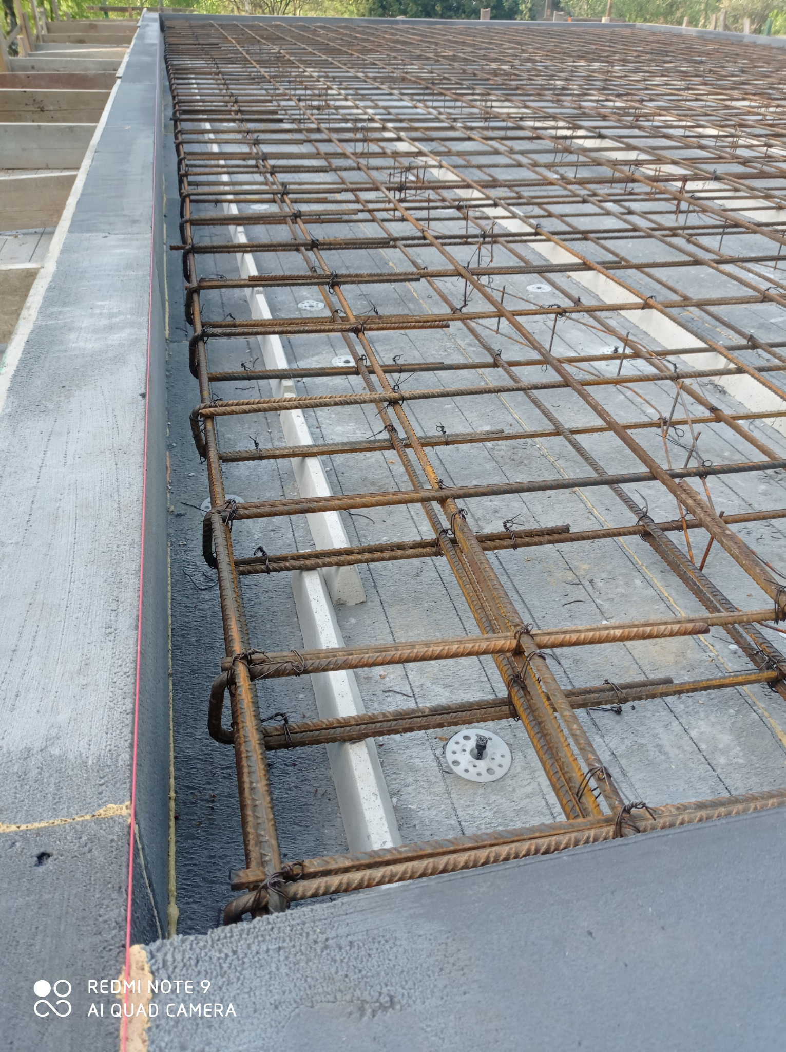 Zbrojenie płyty fundamentowej z widocznymi elementami izolacji termicznej i szalunkiem. Detal z bliska ukazuje siatkę z prętów zbrojeniowych.