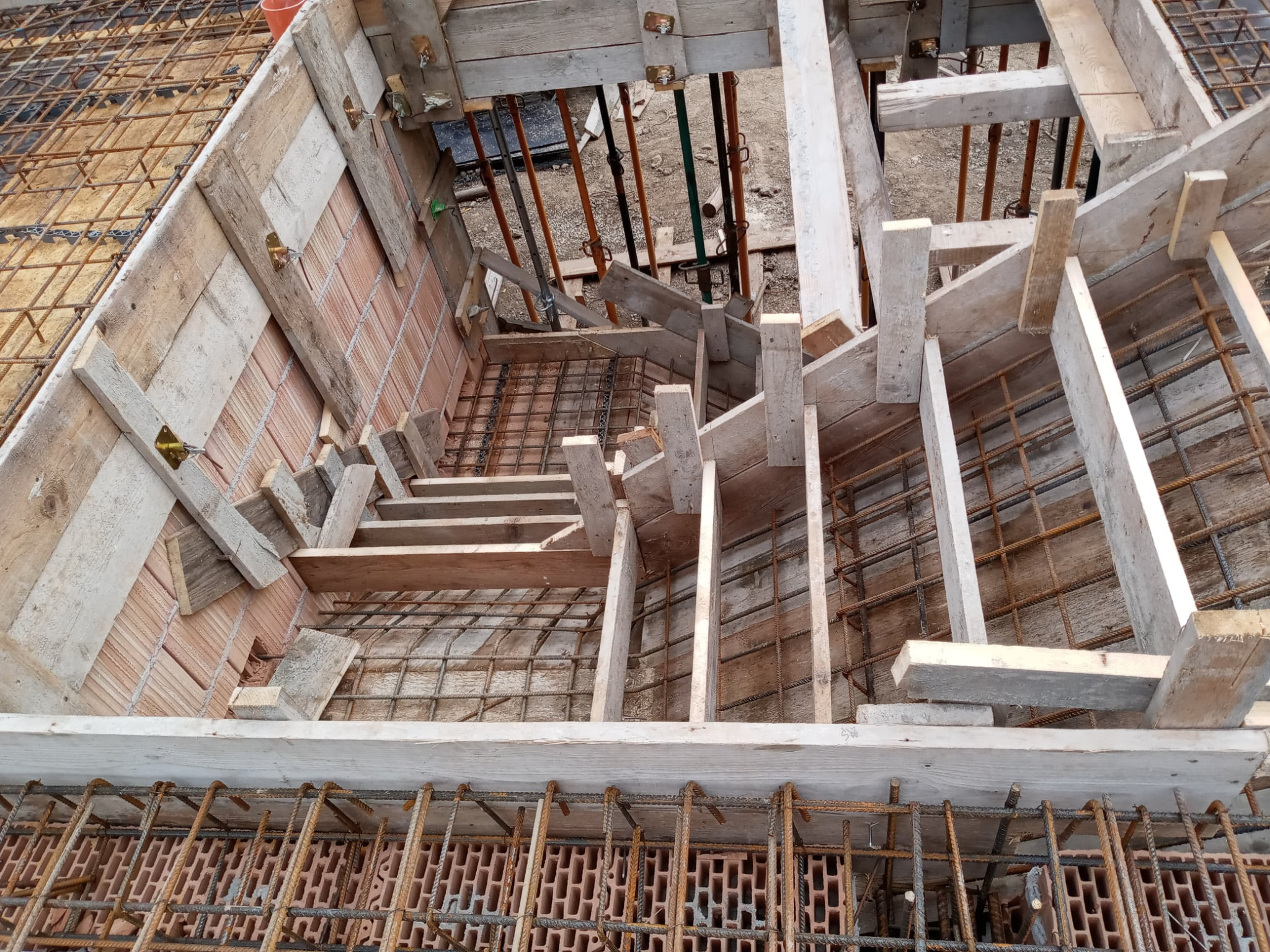 Zbrojenie i szalunek pod fundament. Widok z góry na konstrukcję z drewnianych desek i stalowych prętów, przygotowaną do zalania betonem. Użyto cegieł dziurawek.
