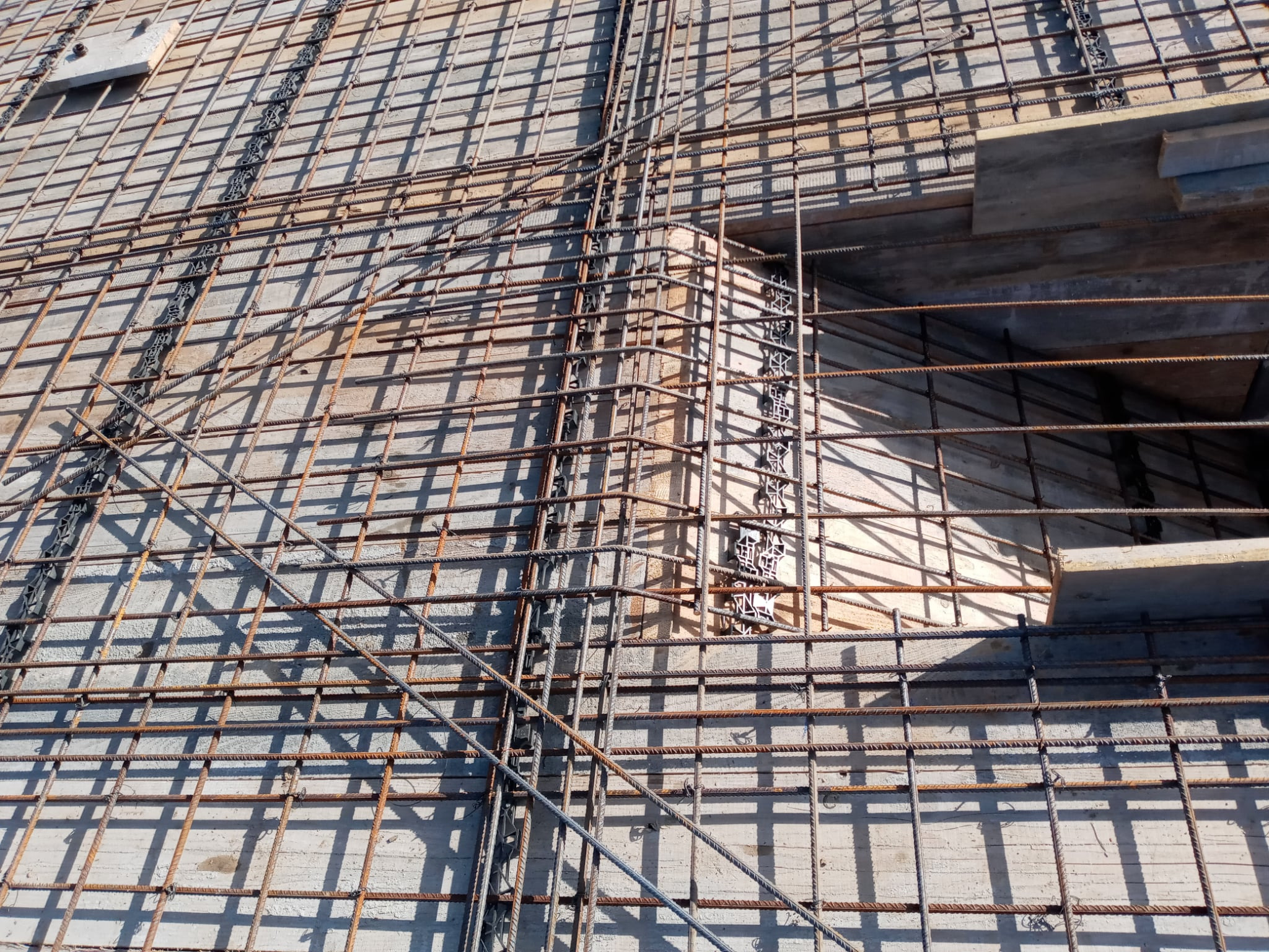 Zbrojenie fundamentu z widocznymi prętami stalowymi ułożonymi w siatkę, przygotowane do zalania betonem. Widoczne elementy szalunku i dystanse z tworzywa.