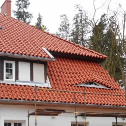 Dachówka klasztorna w kolorze ceglastym na pensjonacie w Kwidzynie, widoczne okna dachowe, małe okrągłe okno na poddaszu, oraz fragment rusztowania i drabina