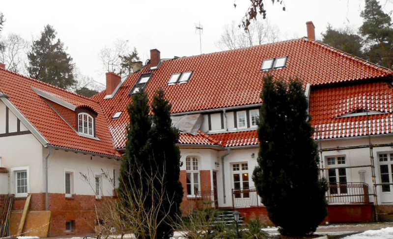 Czerwona dachówka klasztorna na pensjonacie w Kwidzynie, widoczne okna dachowe i kominy.