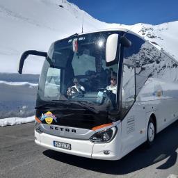 Albatros Travel -wynajem autokarów i busów, przewozy międzynarodowe. - Biały autokar SETRA z logiem Albatros Travel na tle ośnieżonych gór, kierowca w okularach i pasażerowie wewnątrz pojazdu, tablica rejestracyjna G9 USTKA.
