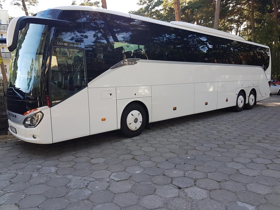 Biały autokar Setra S 517 HD zaparkowany na brukowanym placu, z widocznym budynkiem w tle i drzewami.