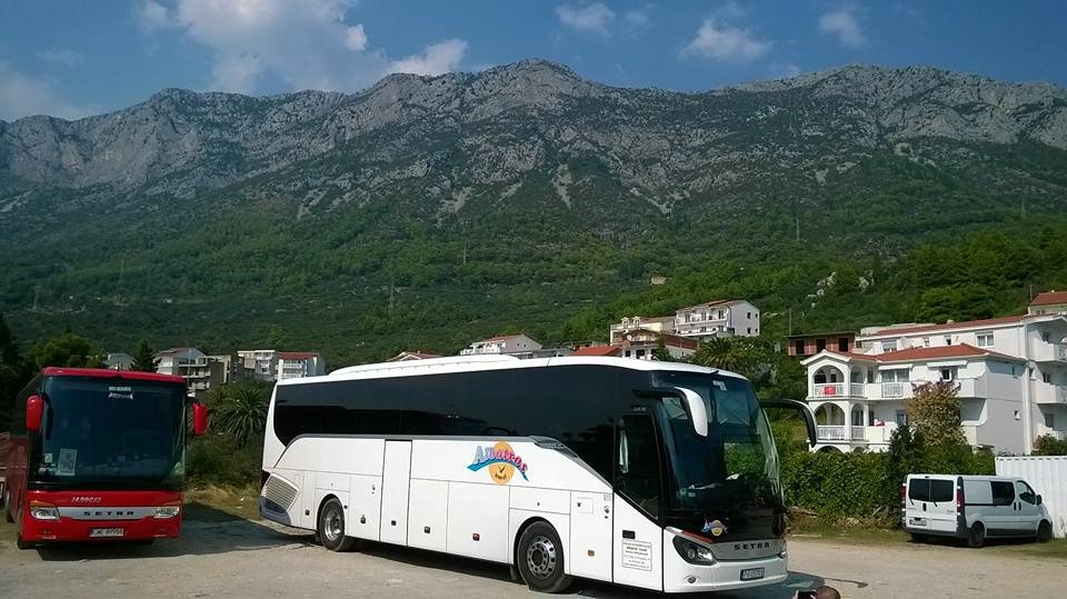 Dwa autokary Setra, czerwony i biały z logo Albatros, zaparkowane na tle górskiego krajobrazu i zabudowań mieszkalnych.