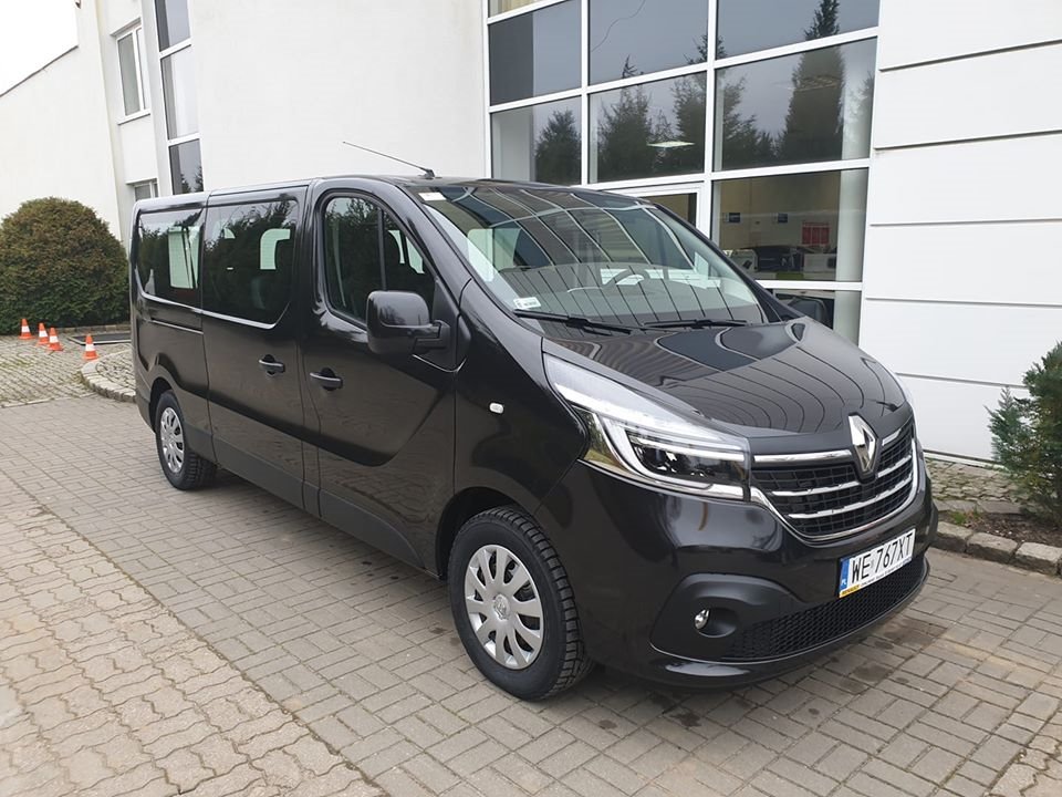 Czarny van Renault Trafic z polską tablicą rejestracyjną zaparkowany przed nowoczesnym budynkiem biurowym z dużymi oknami.